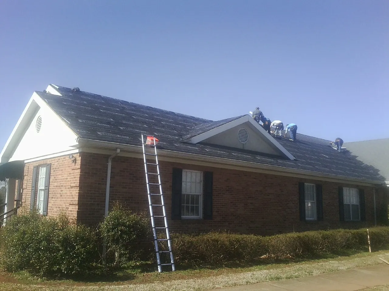 Crew tearing shingles off a brick ranch roof with a ladder set — Metal Roof Repair work by our crew in Rolla