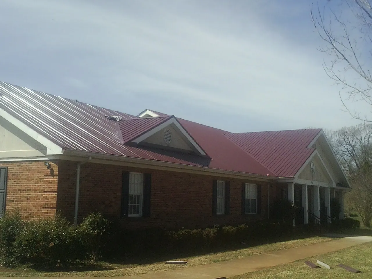 Red metal roof with gabled entries on a long brick building, from a Hail Damage Roof Repair job in Rolla