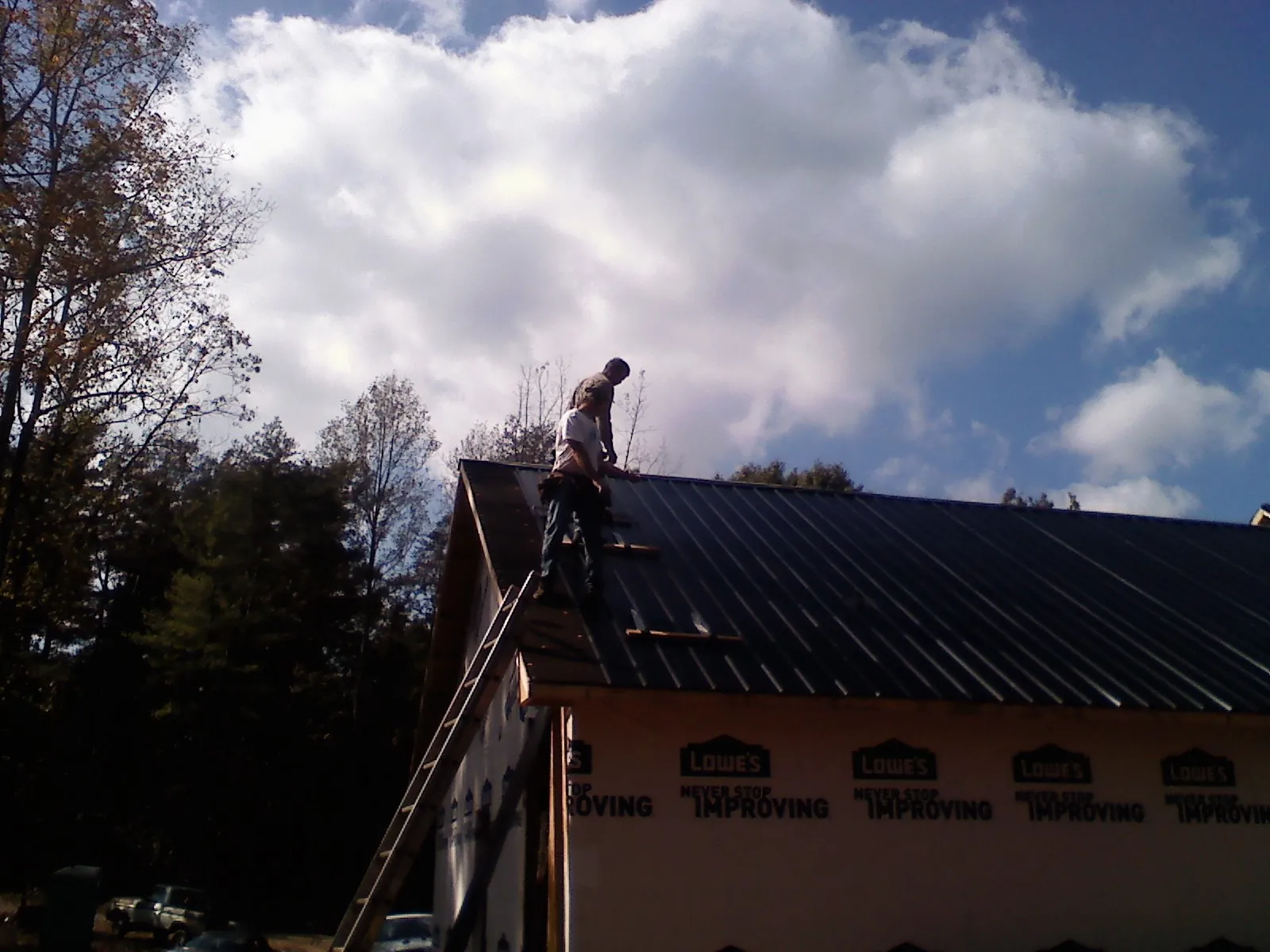 Roofer fastening dark metal panels high against a cloudy sky, from a Roof Inspection job in Rolla