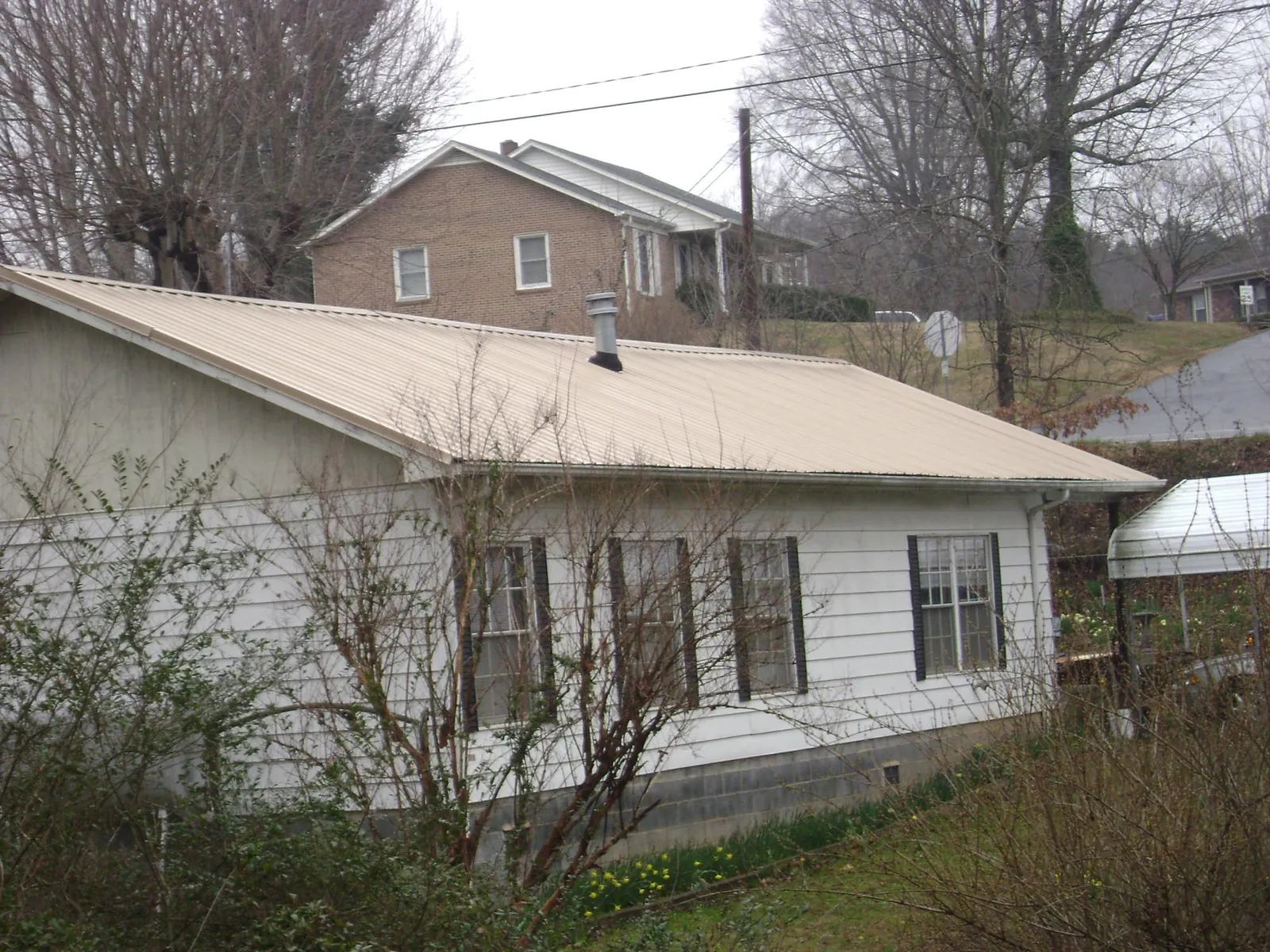 Tan metal roof on a white sided house set into a hillside — Commercial Roofing by Roofing Brothers in Rolla