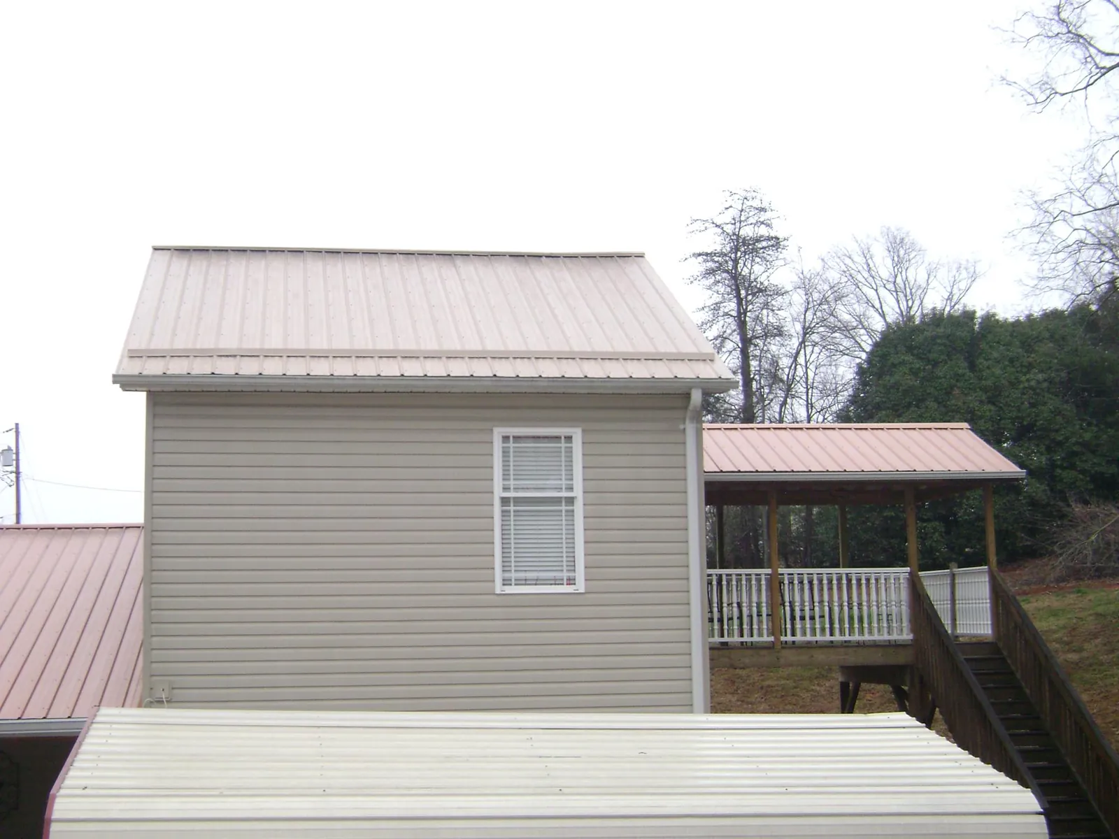 Tan metal roofs on a two story addition and attached porch, from a Roof Replacement job in Rolla